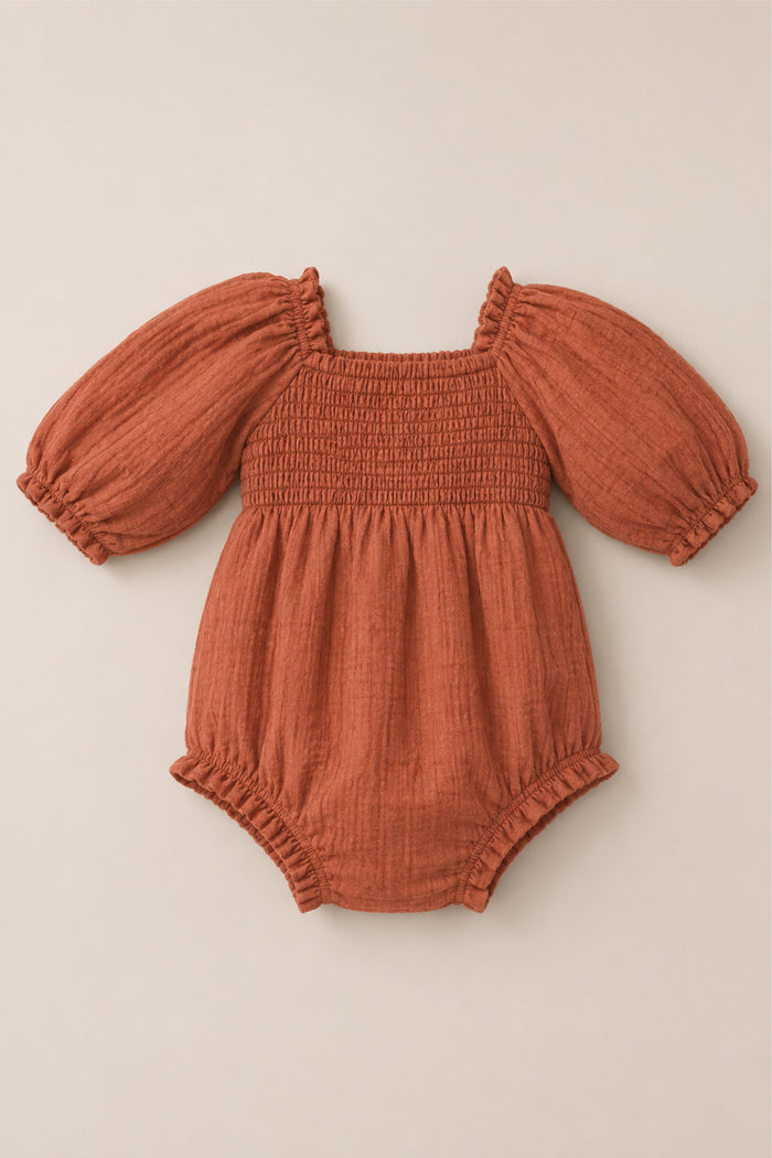 The Ivy City Co Baby Madeline Romper in Apple Cider, featuring puff sleeves, a smocked bodice, and ruffled edges, is laid flat on a neutral background.