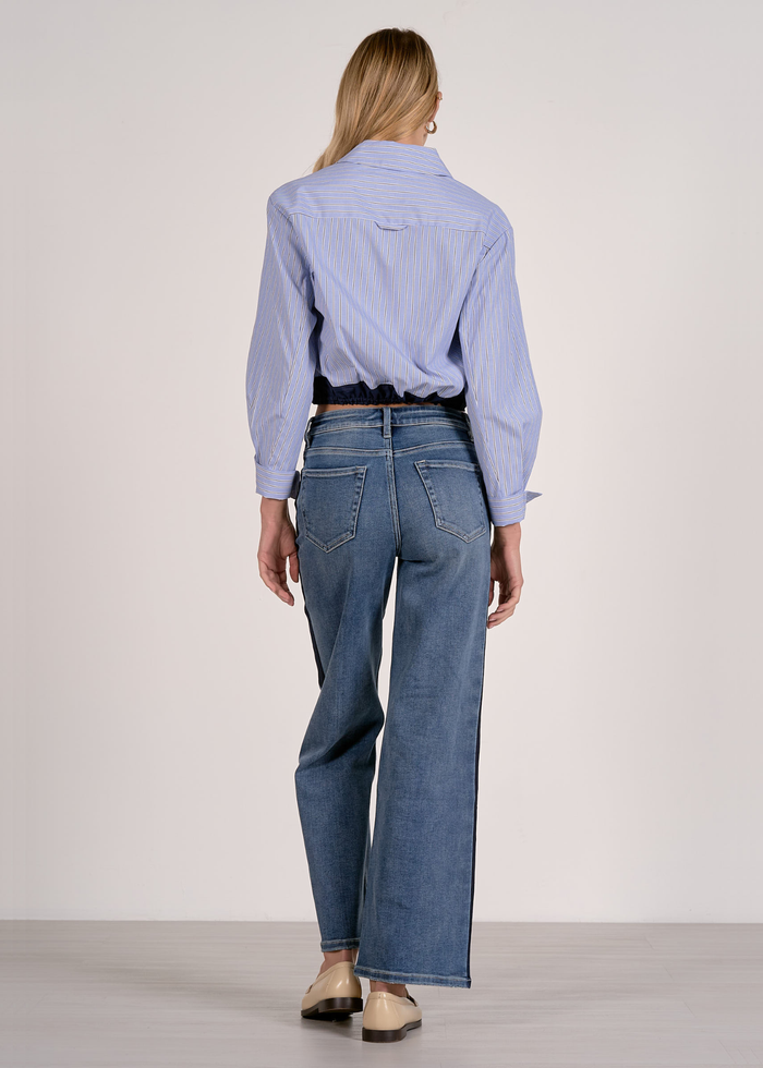 Woman turned around wearing a blue stripe button down with a navy cinched waistline and jeans