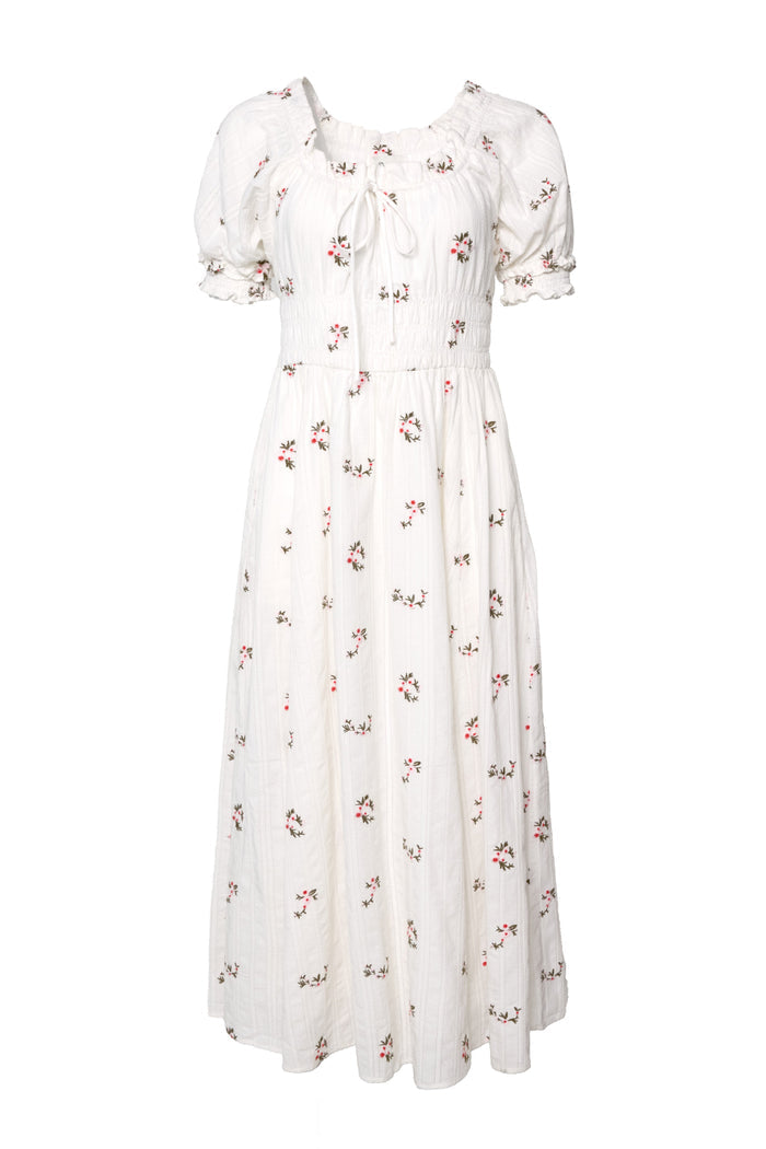The Jessie Dress in Ditsy Embroidery by Ivy City Co is a white, ankle-length cotton dress featuring short sleeves, a smocked bodice, ruffled neckline, and scattered small floral embroidery.