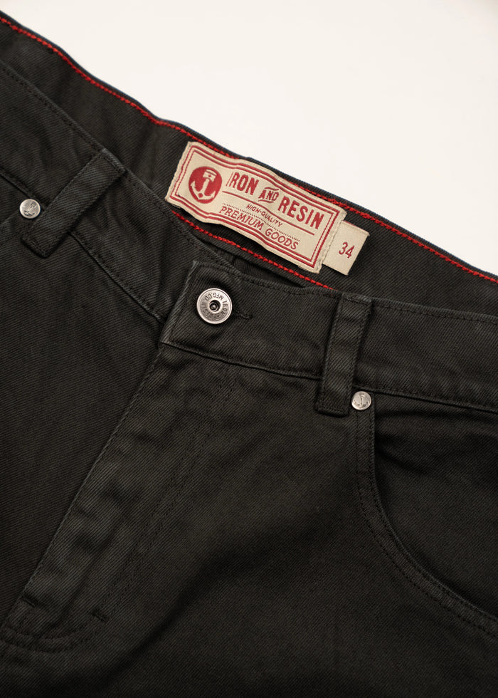 Close-up of black jeans with a red label reading "Iron and Resin Premium Goods" and size 34, showcasing quality denim details.