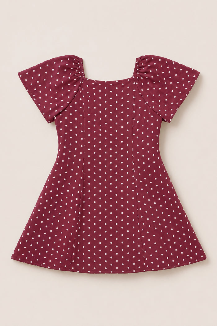 A Teen Blakely Dress in Cranberry Dainty Dot by Ivy City Co, featuring white polka dots, puffed petal sleeves, and a fitted waist, is laid flat on a light background.