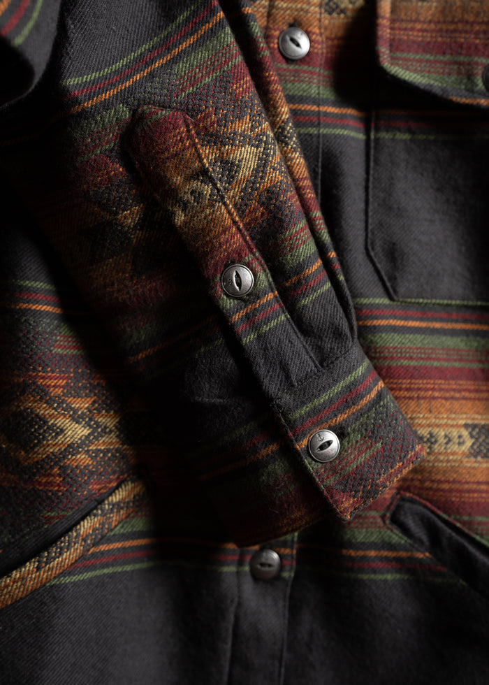 Close-up of a plaid wool jacket with metal buttons, featuring red, green, and orange stripes in a classic pattern.