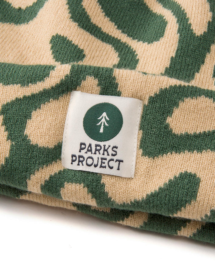 Close up of Yellowstone Geysers beanie knit in beige and green camo with a Parks Project tag featuring a pine tree
