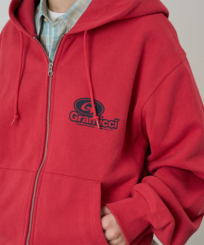 Model wearing a Gramicci crimson red '82 Zip Hooded Sweatshirt with black graphic against a light tone background.