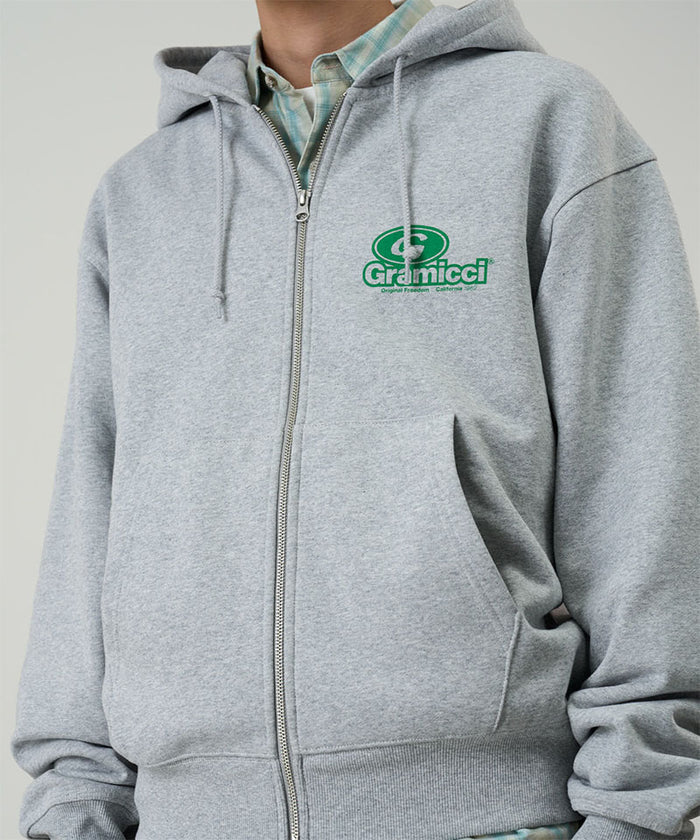Model wearing a Gramicci heather grey '82 Zip Hooded Sweatshirt with green graphic against a light tone background.