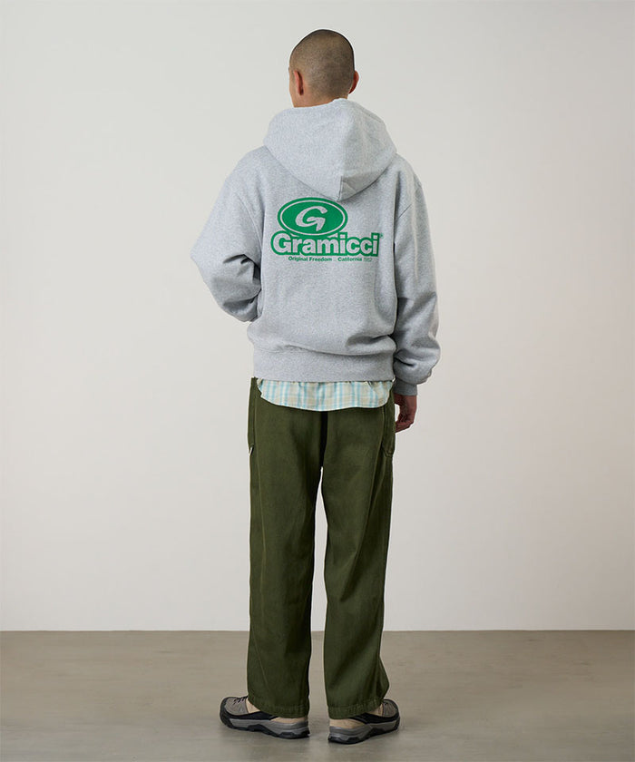 Back view of a model wearing a heather grey Gramicci '82 Zip Hooded Sweatshirt with a green graphic and green pants on a light tone background.