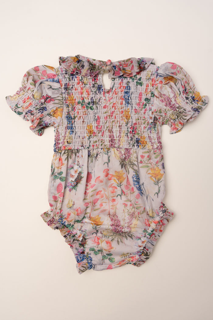 The Ivy City Co Baby Cordelia Floral Romper has a delicate floral print, short ruffled sleeves, smocked bodice, and gathered leg openings, displayed flat on a plain light background.