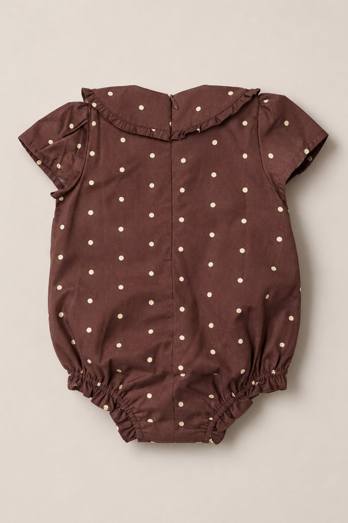 The Ivy City Co Baby Kit Romper in Warm Cocoa Dainty Dot features short sleeves, a charming Peter Pan collar, and cream polka dots. Crafted from soft cotton, this romper includes elastic leg openings and a convenient back zipper, all displayed flat on a neutral background.