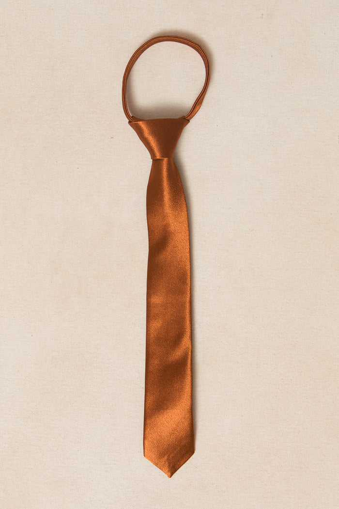 The Ivy City Co Boys Max Tie in Amber Satin, featuring an adjustable zipper knot and loop, is displayed flat on a light beige background.