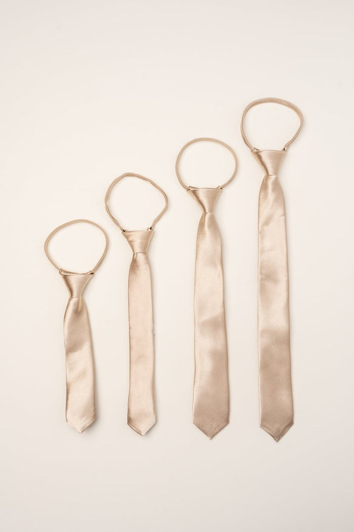 Four Boys Max Ties in Champagne by Ivy City Co are arranged in a row on a light background, each tied with a simple knot and their loops positioned above—making them the perfect stylish accessory for boys and an elegant choice for weddings.