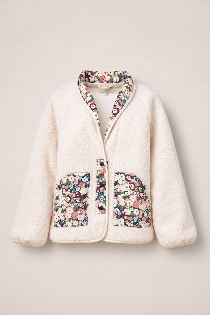 The Britta Jacket in Ivory & Midnight Garden by Ivy City Co is an ivory sherpa jacket featuring quilted floral trim along the collar, placket, and two front pockets—an effortlessly versatile piece for your fall wardrobe. Shown against a plain light background.
