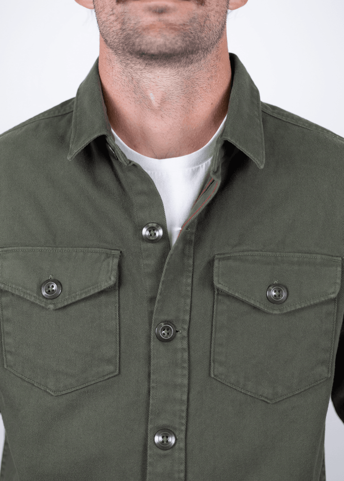 Man wearing a green button-up shirt with two chest pockets over a white t-shirt, focusing on upper torso and shirt details.