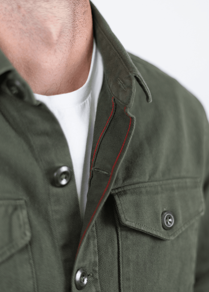 Close-up of a green jacket with black buttons and red stitching, worn over a white shirt.