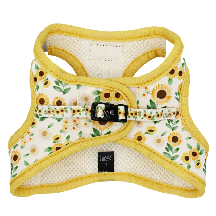 The Sassy Woof Cat Step-In Harness - Sunflower Dreams features yellow trim, a sunflower and green leaf pattern, reflective strips for safety, a black buckle, and a Sassy Meow label at the bottom center.