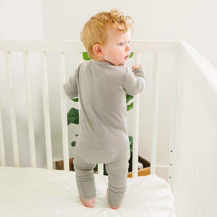 Baby in a Dove-colored footless baby romper standing in a crib.