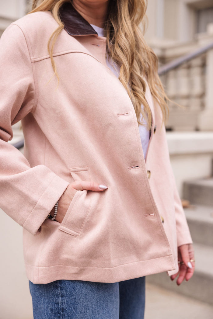 A woman wearing the Ivy City Co Daphne Coat in Light Pink with one hand in her pocket, paired with blue jeans; background features stairs and a railing.