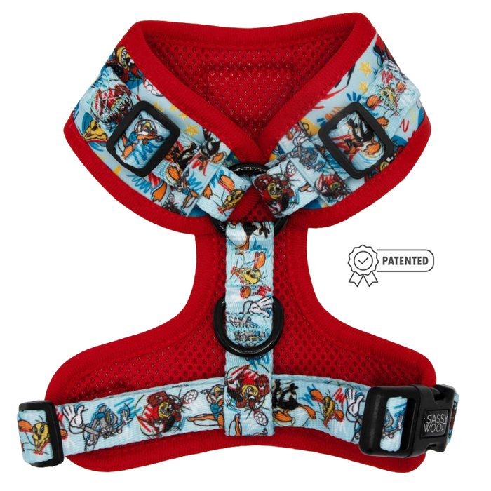 The Sassy Woof Dog Adjustable Harness - Looney Tunes™ Blue features cartoon character designs, black adjustable buckles, D-rings, custom-printed neoprene material, and a small PATENTED badge near the brand name.