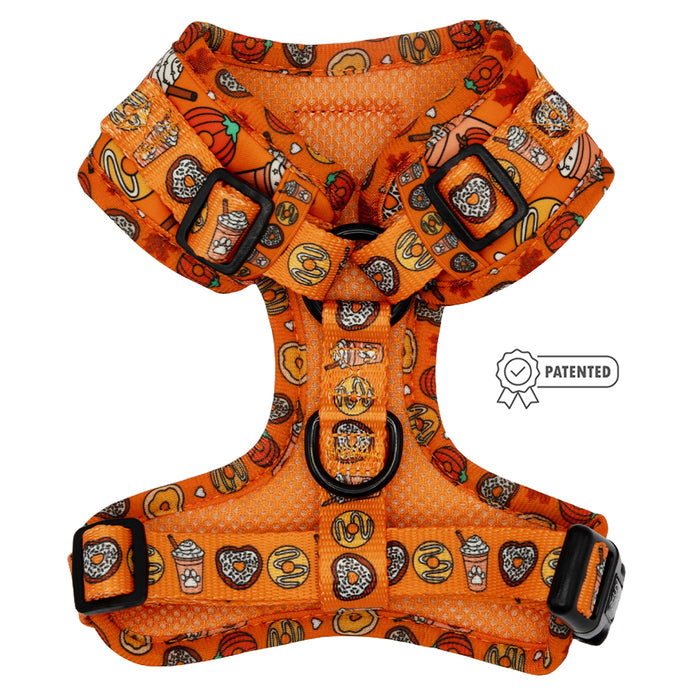 The Sassy Woof Dog Adjustable Harness - Pupkin Donuts features an orange design with black buckles and a playful print of pumpkins, coffee cups, donuts, and pretzels—perfect for autumn. A patented badge icon appears to the right of the harness.