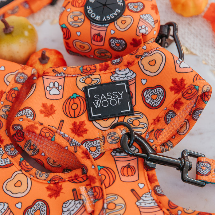 Close-up of the Sassy Woof Dog Adjustable Harness - Pupkin Donuts, featuring vibrant orange colors and playful autumn designs like pumpkins, leaves, coffee cups, paw prints, and donuts. Small apples appear in the background.