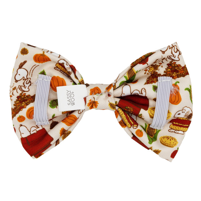 The Sassy Woof Dog Bowtie - Peanuts™ Harvest features autumn and Thanksgiving illustrations—pumpkins, pies, bread, and leaves—on a white fabric with gray loops and a center tag. Perfect for festive dog accessories.