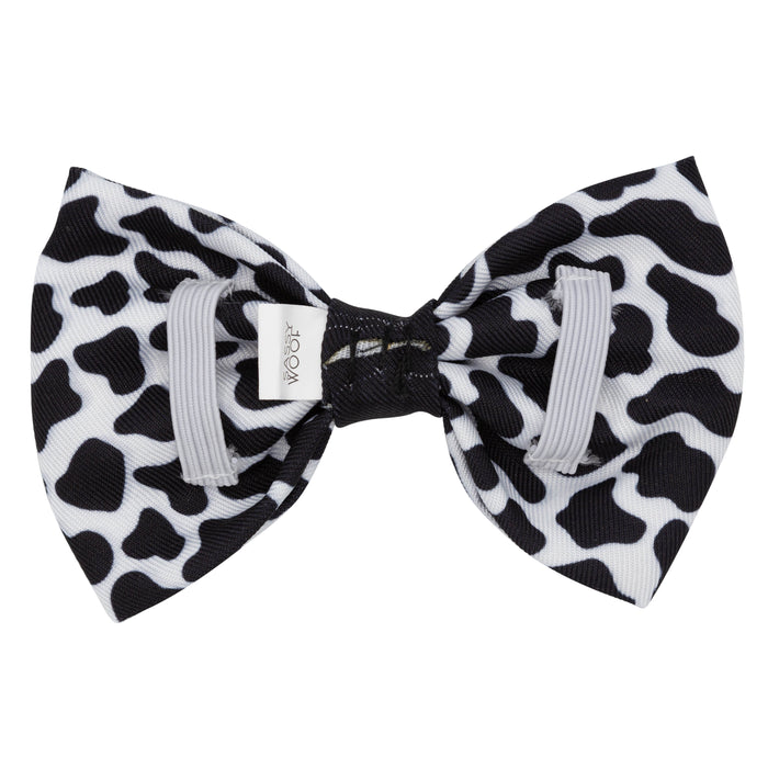 The Dog Bowtie - Whole Milk by Sassy Woof is a stylish pet accessory featuring a black and white cow print design, two light gray bands, and a small white tag on the left side—perfect for adding a playful touch to your furry friend’s look.
