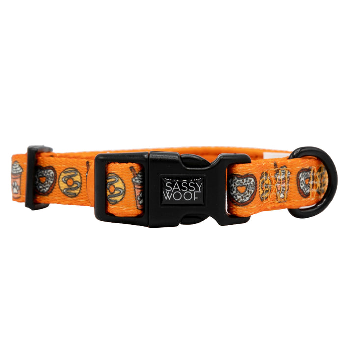 The Dog Collar - Pupkin Donuts by Sassy Woof is an orange neoprene collar with a black plastic buckle, adjustable fit, and whimsical donut and heart designs. Features the Sassy Woof logo in white—ideal for fall-loving pups.