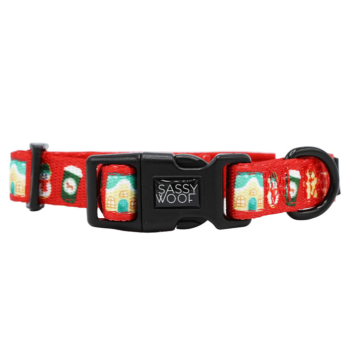 The Sassy Woof Dog Collar - Sleigh Baby Sleigh features festive gingerbread house and stocking designs, a red adjustable strap, and a black plastic buckle—perfect for adding holiday style to your dog's accessories.