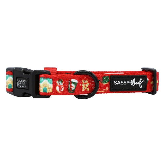 The Sassy Woof Dog Collar - Sleigh Baby Sleigh features red holiday designs with houses, snowmen, and trees. Adjustable with a black buckle and circular ring, it's the perfect festive accessory for your pup.
