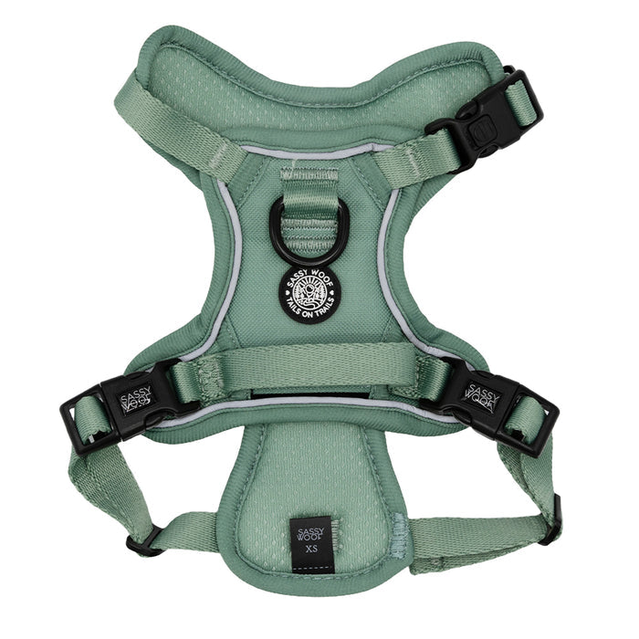 The Sassy Woof Dog Step-in Harness in sage green features black buckles, adjustable straps, and a round patch at the top center. Shown flat on a white background, this padded harness blends style and function for your pup.