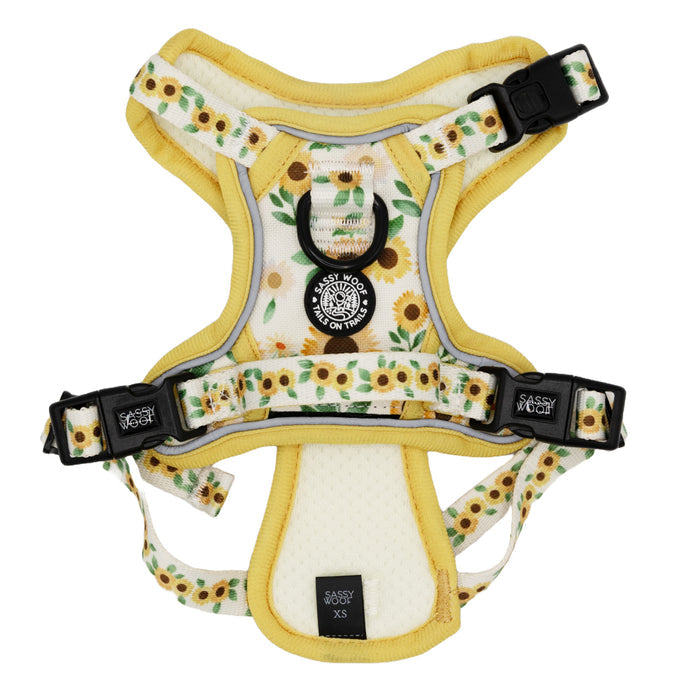 The Sassy Woof Dog Step-In Harness - Sunflower Dreams features a sunflower pattern, yellow trim, black buckles, reflective straps, an adjustable fit, and a front label that reads Sassy Woof.