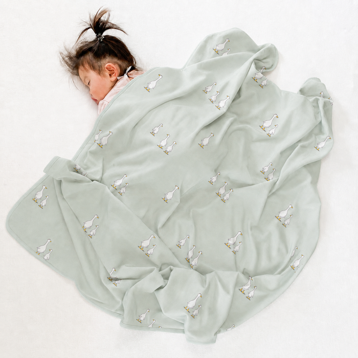 Sleeping child covered with a light green blanket with goose patterns on a white background