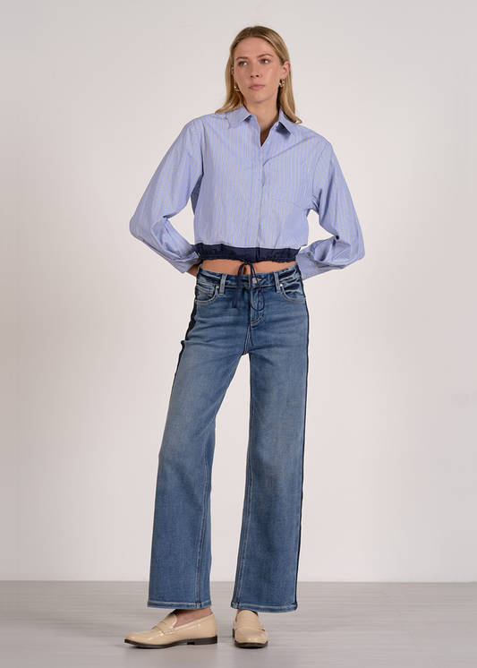 Woman wearing a blue stripe button down with a navy cinched waistline and jeans