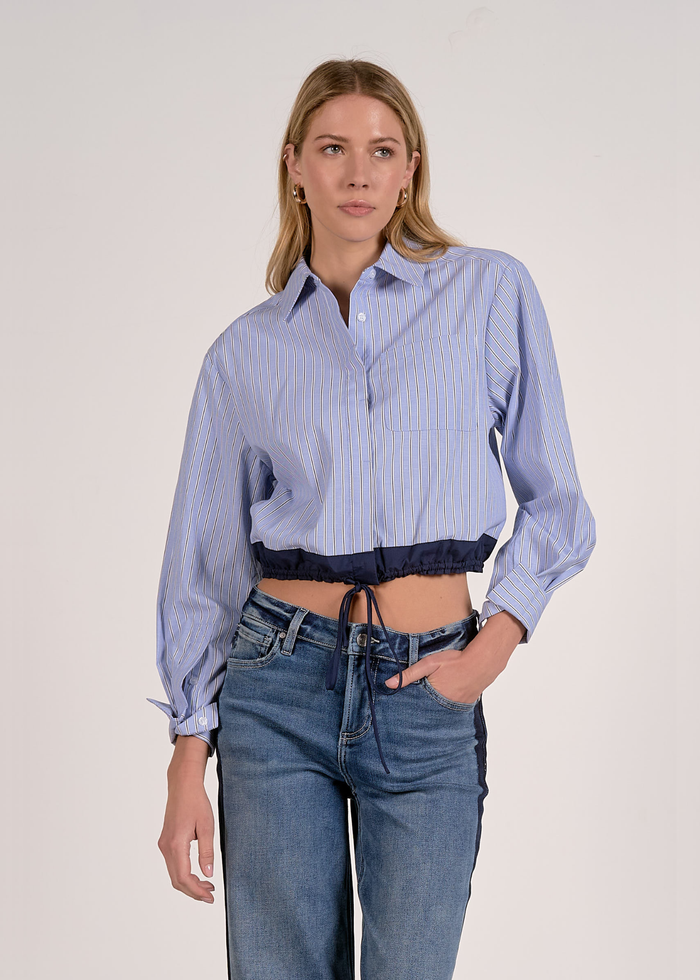 Woman wearing a blue stripe button down with a navy cinched waistline and jeans