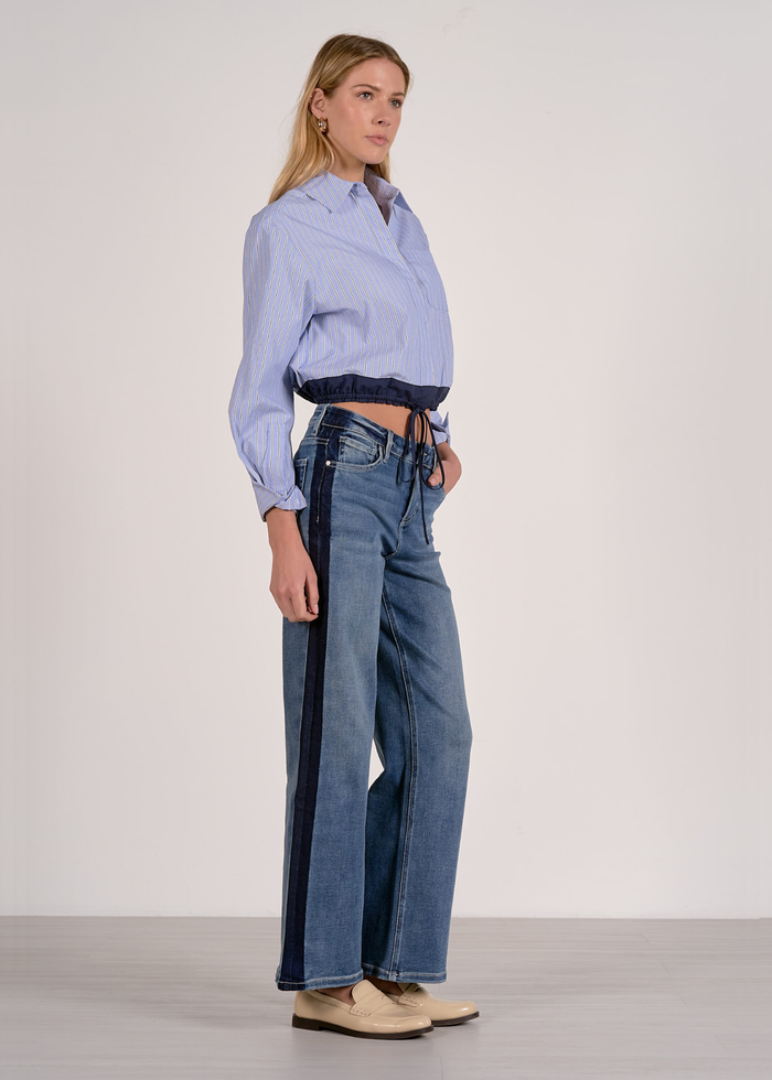 Woman turned to the side wearing a blue stripe button down with a navy cinched waistline and jeans