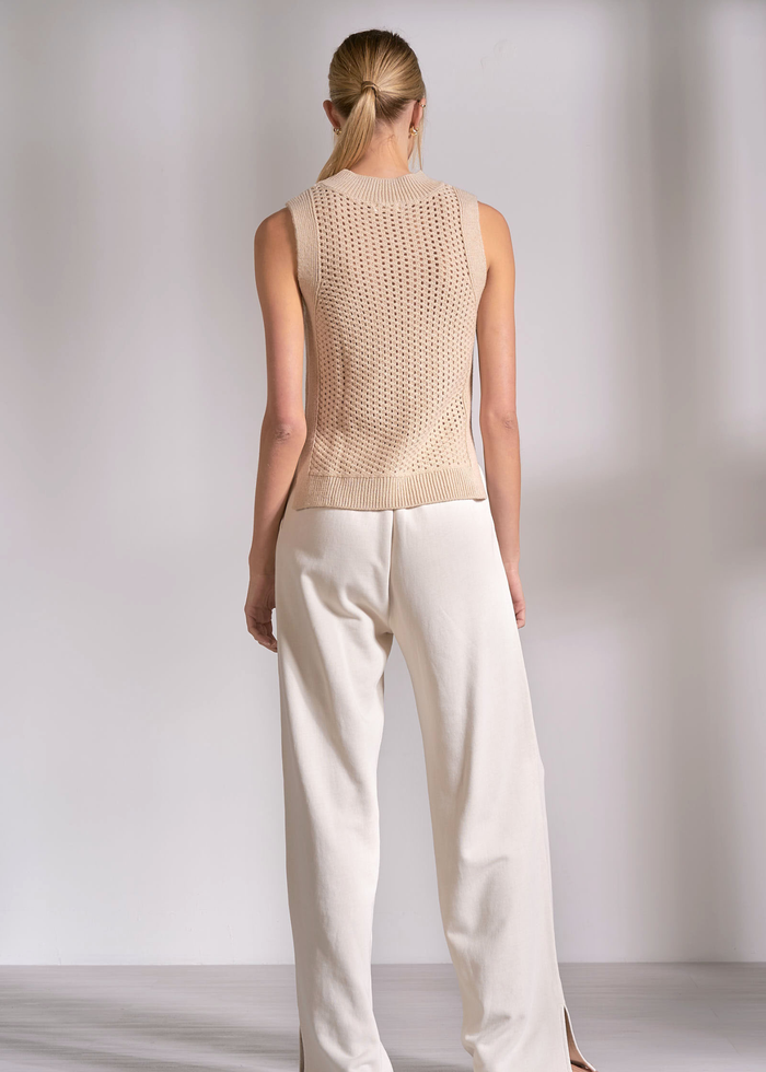 Woman turned around wearing a tan knit tank top with cream pants
