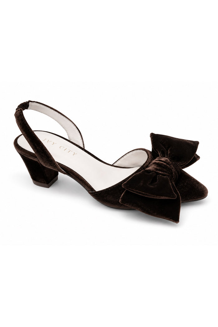 The Eloise Bow Heel in Brown by Ivy City Co features a low block heel, a stylish slingback design, and an oversized bow detail on the toe. Crafted with supple leather lining for all-day comfort, this elegant brown velvet shoe is displayed on a white background—twirl-ready and perfect to pair with your favorite dress.