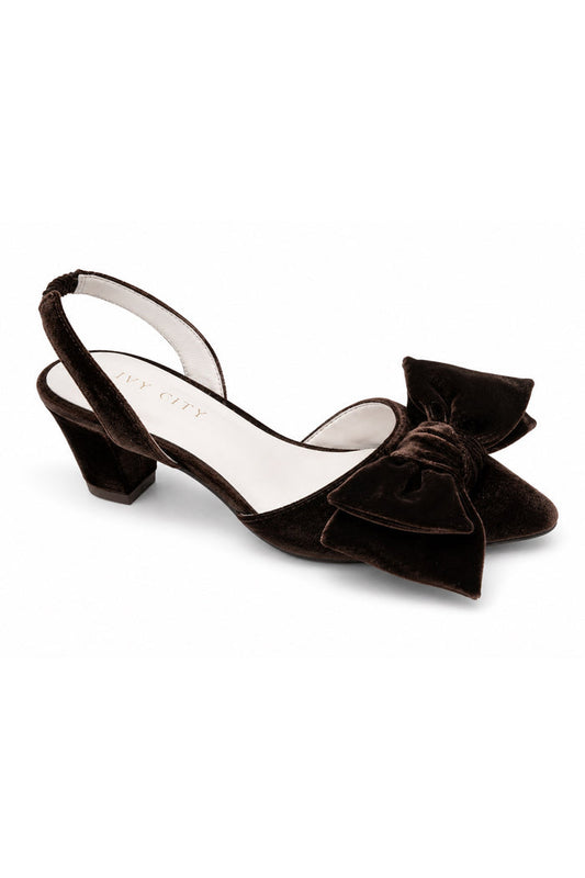 The Eloise Bow Heel in Brown by Ivy City Co features a low block heel, a stylish slingback design, and an oversized bow detail on the toe. Crafted with supple leather lining for all-day comfort, this elegant brown velvet shoe is displayed on a white background—twirl-ready and perfect to pair with your favorite dress.