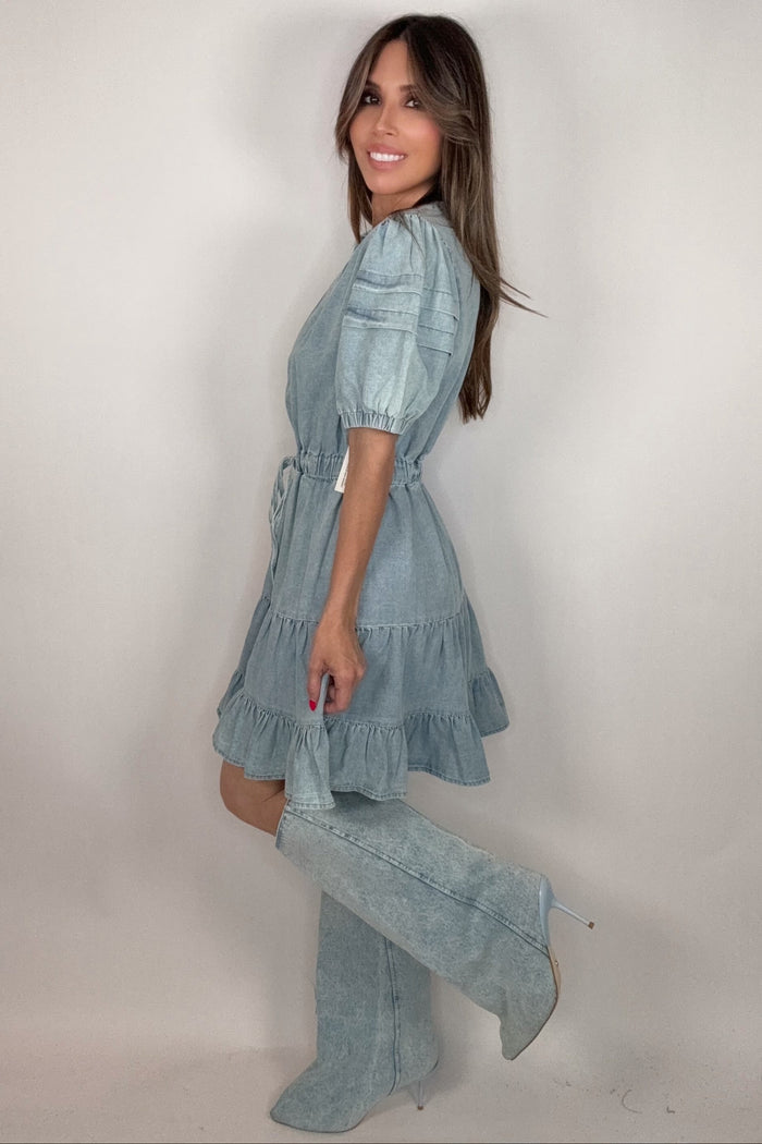 Washed denim mini dress with a ruffle neckline, puff sleeves, elastic waist, and tiered skirt.