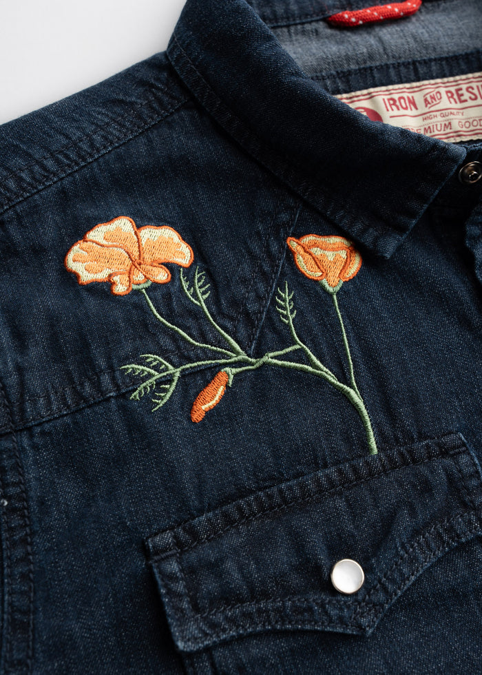 Denim shirt with orange poppy embroidery above the pocket, showcasing intricate floral design and button detail.