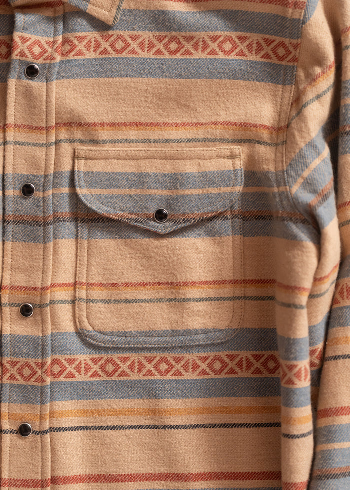 Close-up of a beige flannel shirt with blue and red stripes, featuring a front pocket and black buttons.