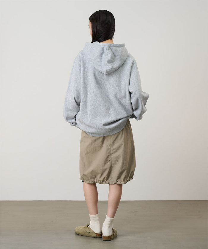Back view of a model wearing a heather grey Gramicci G-Flower Hooded Sweatshirt and beige skirt on a light-tone background.
