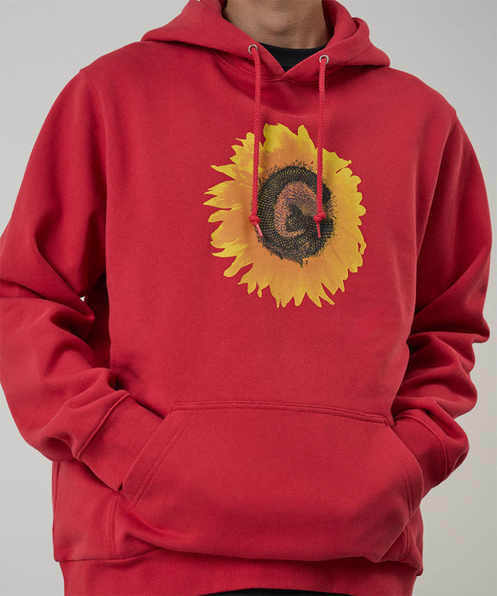 Model wearing a Gramicci crimson red G-Flower Hooded Sweatshirt with a sunflower graphic against a light-tone background.