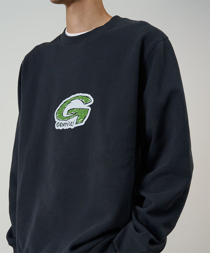 Model wearing a Gramicci vintage black G-Scribble Sweatshirt with green graphic against a light tone background.