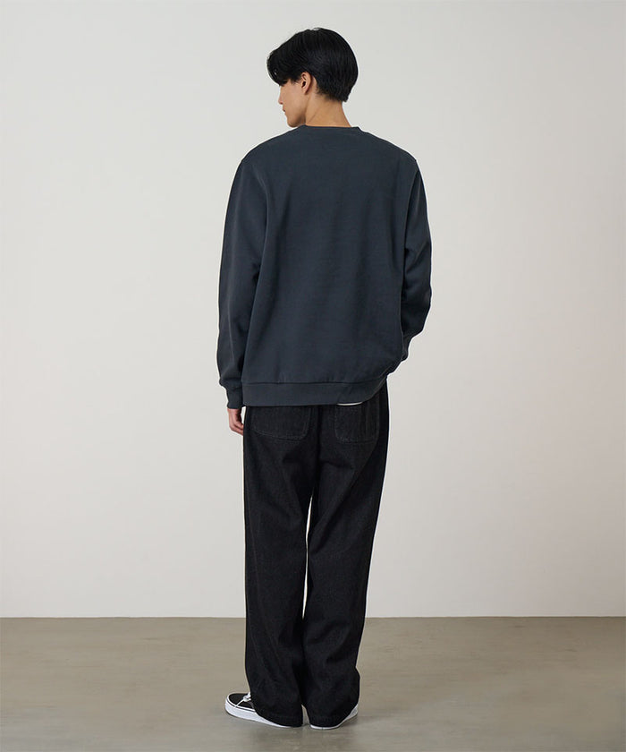 Back view of a model wearing a vintage black Gramicci G-Scribble Sweatshirt and black pants on a light tone background.