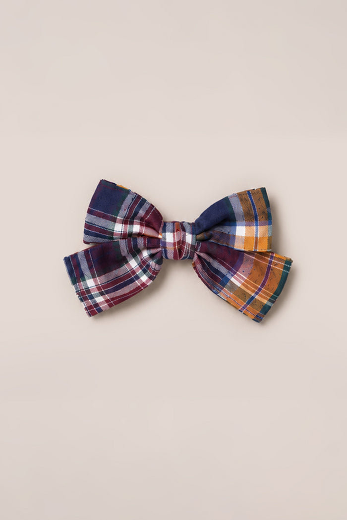 Introducing the Hair Bows in Midnight Plaid by Ivy City Co—crafted from cotton and showcasing a timeless plaid pattern with dark blue, red, white, yellow, and orange stripes. This elegant hair bow is securely fastened to a French barrette clip and photographed against a plain light beige background.