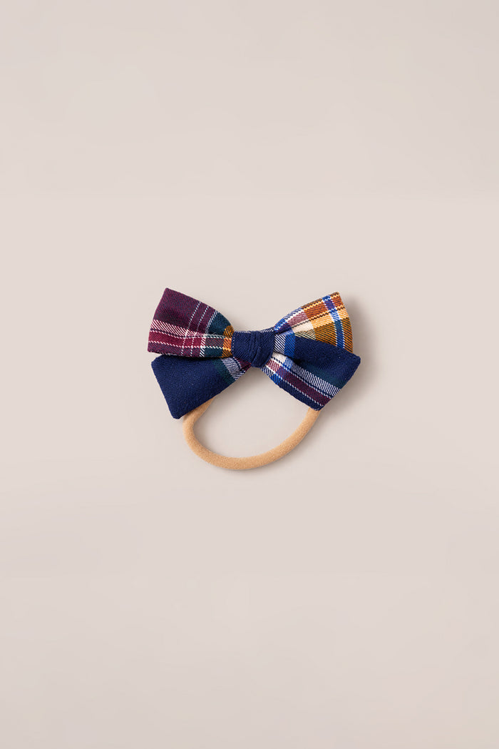 The Ivy City Co Hair Bows in Midnight Plaid feature soft cotton fabric with blue, maroon, and yellow plaid patterns. Each bow is attached to a beige elastic hair tie and showcased against a light beige background.