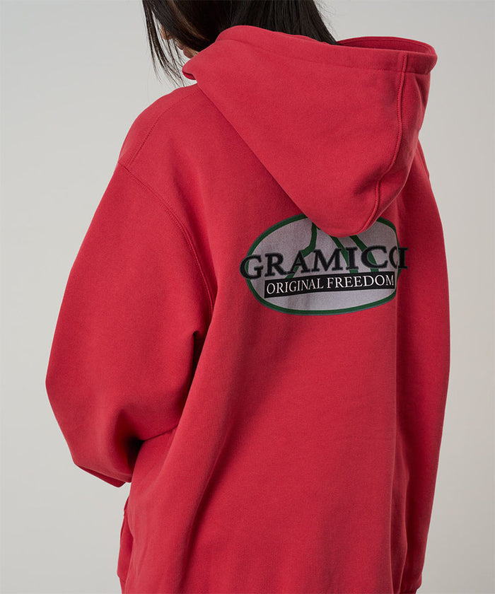 Back view of a model wearing a crimson red Gramicci Half Dome Hooded Sweatshirt on a light tone background.