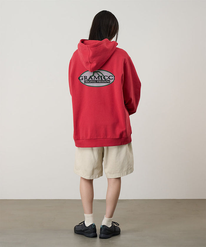 Back view of a model wearing a crimson red Gramicci Half Dome Hooded Sweatshirt with a beige and green graphic and beige shorts on a light tone background.
