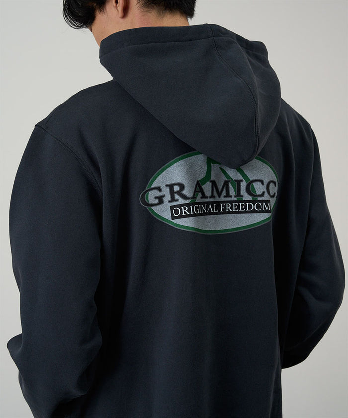 Back view of a model wearing a Gramicci vintage black Half Dome Hooded Sweatshirt with beige and green graphic against a light tone background.