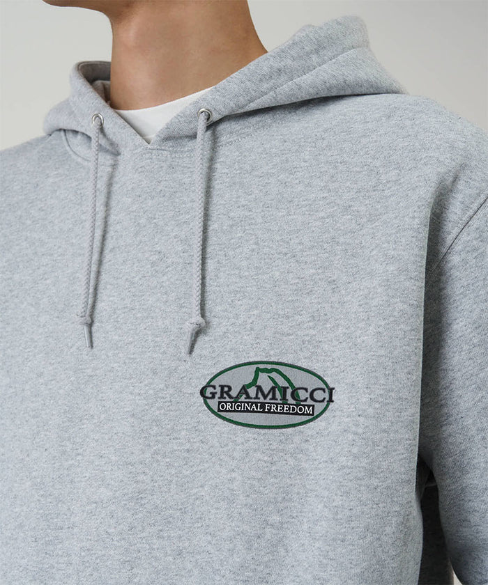 Model wearing a Gramicci heather grey Half Dome Hooded Sweatshirt with beige and green graphic against a light tone background.